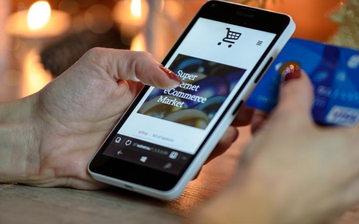 Een mobiele telefoon in de handen van een vrouw. Op de telefoon is een webshop geopend.