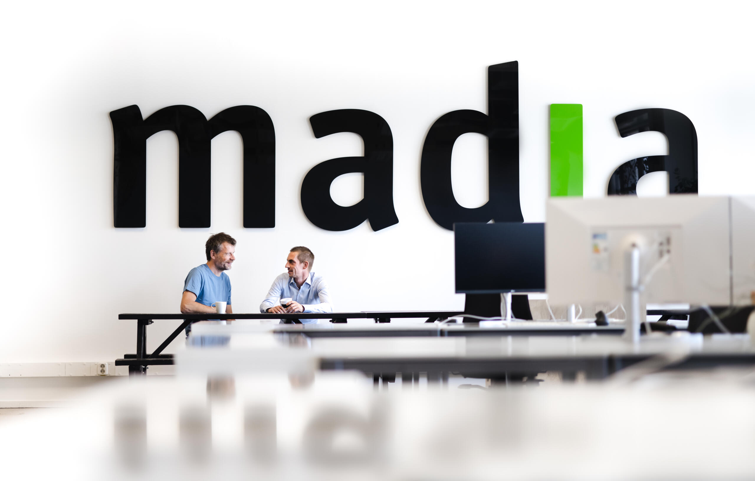 Two teammembers of Madia in front of the Madia logo