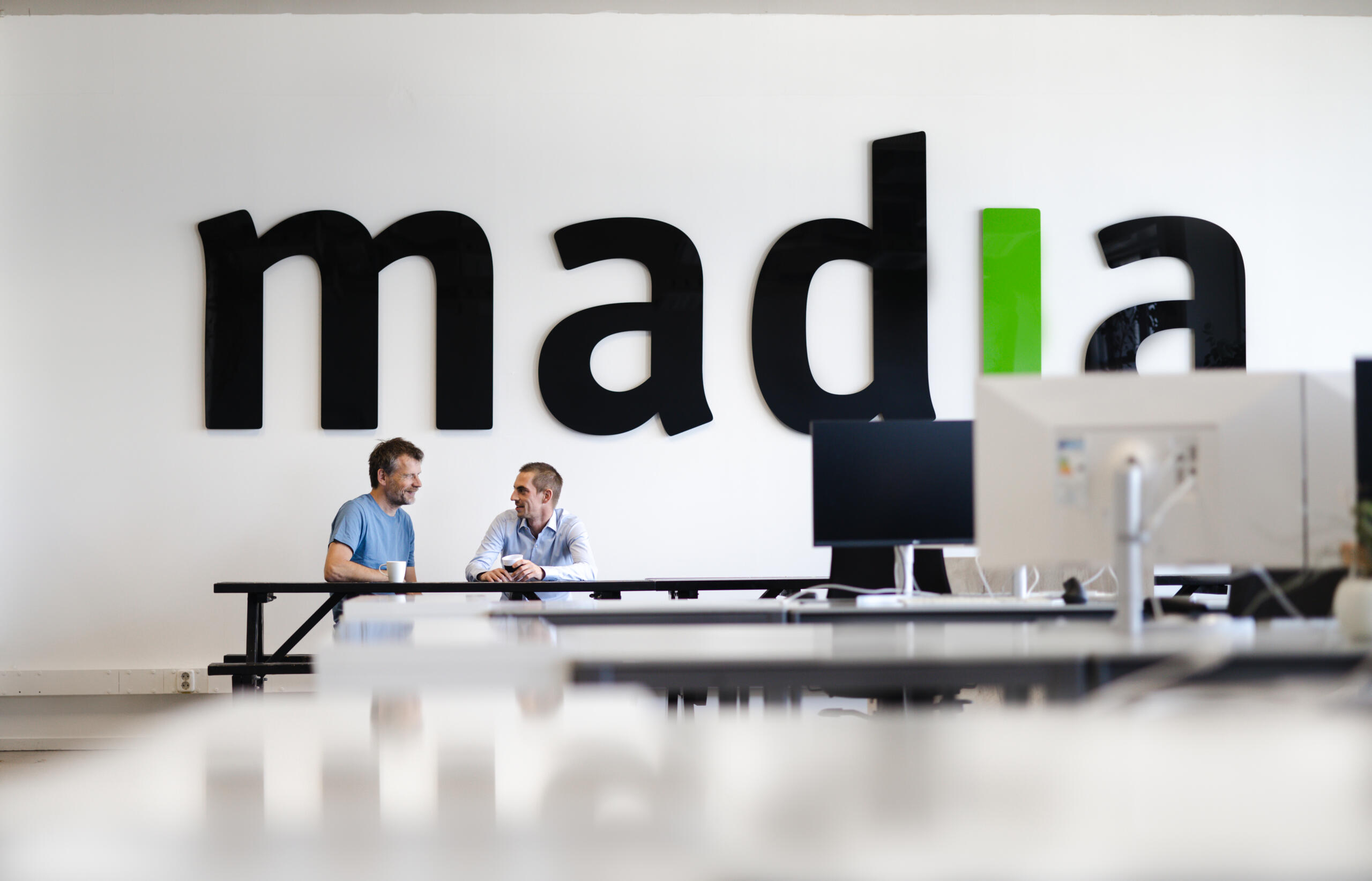 Two people in front of the Madia logo